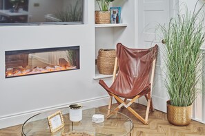 Relax in a serene space with a comfortable leather armchair, fireplace, and lush greenery.