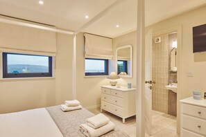 Relax in a spacious room with a large bed, bedside table, and dresser, offering a view of the outdoors through two windows.