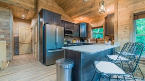 A modern kitchen with wooden walls, stainless steel appliances, and a central island with bar stools. - Fun and Funner! Family cabin with mountain view and pinball! (Sevierville)