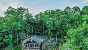 A two-story wooden cabin surrounded by dense forest. - Fun and Funner! Family cabin with mountain view and pinball! (Sevierville)