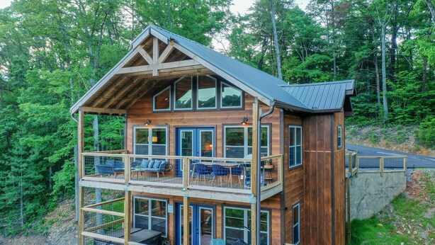 A multi-story wooden cabin with balconies, large windows, and a metal roof, surrounded by forest. - Fun and Funner! Family cabin with mountain view and pinball! (Sevierville)
