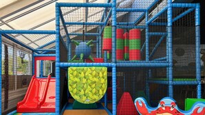 Ein Kinderspielbereich mit Rutsche, Kletternetz und einem Krabben-Tunnel.