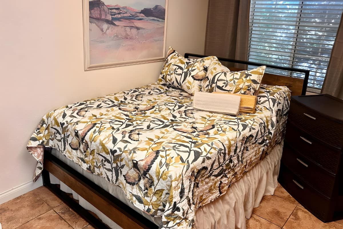 A bedroom with a bed, a nightstand, a dresser, and a window with blinds.