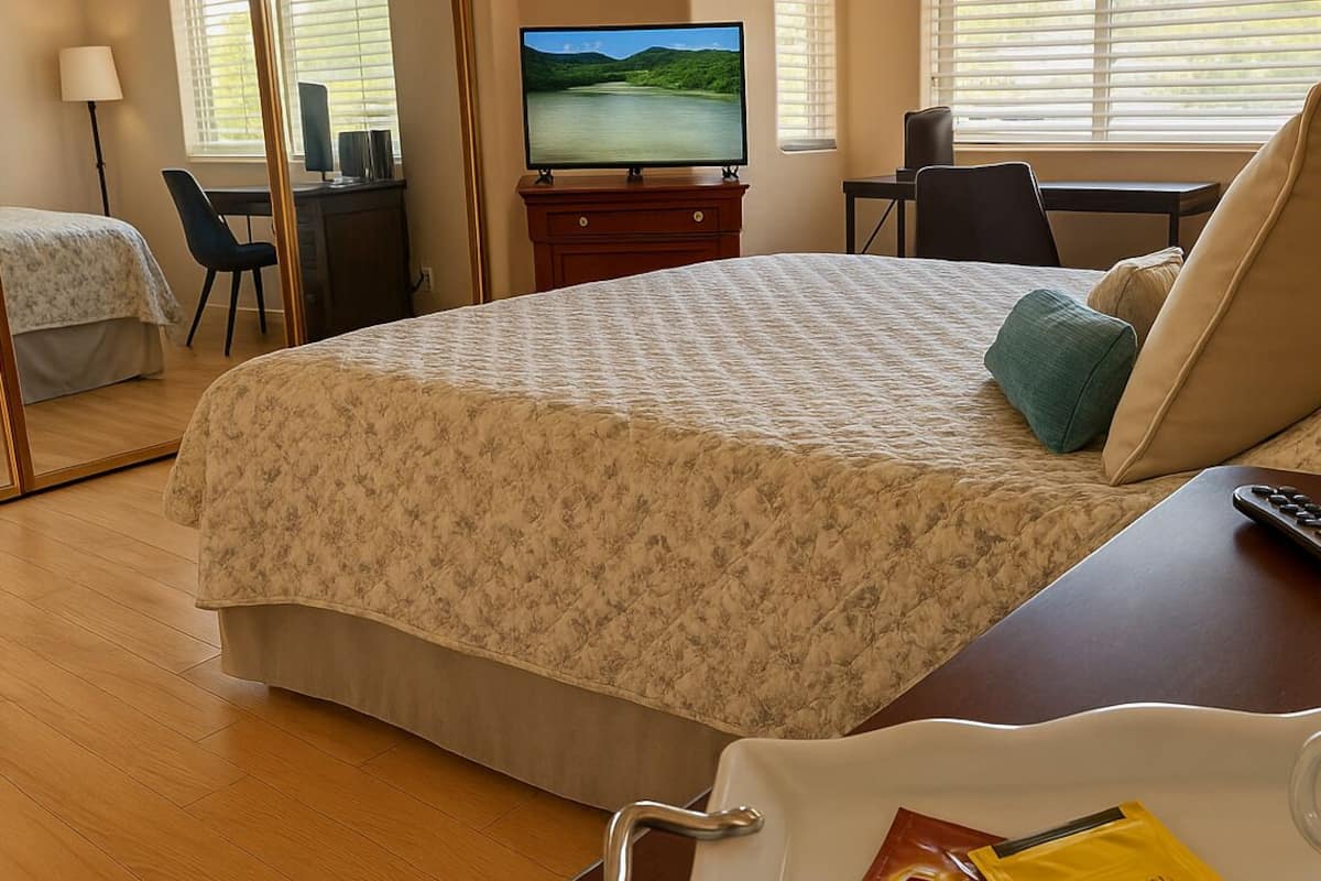 A hotel room with a large bed, a desk with a computer, a television, and a coffee table with a remote control and a glass.