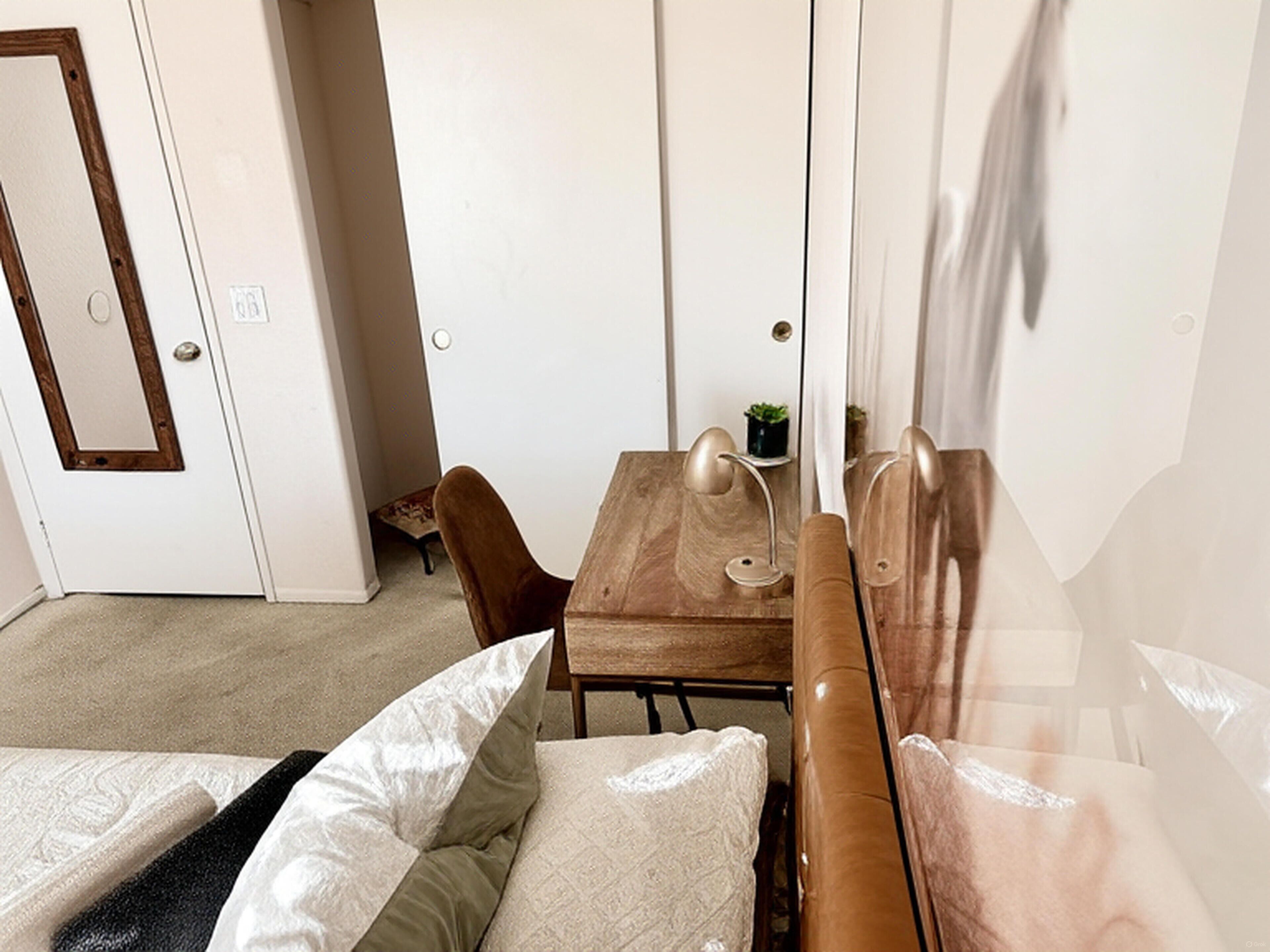 A room with a bed, a wooden table with two chairs, a small potted plant, and a mirror on the wall.