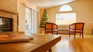 A living room with a wooden dining table, two wooden chairs, a Christmas tree, a fireplace, and a large window. - Private bedroom in Western Horizon Home (Hemet)