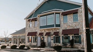 A two-story stone building with a green roof and red awnings, featuring a large bay window and a stone facade. - GrueneGusthaus#1| Private Condo +Golf Cart Rentals (New Braunfels)