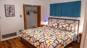 Quarto com cama, mesa de cabeceira, luminária, guarda-roupa e um quadro na parede.