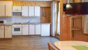 Una cocina compacta con electrodomésticos blancos, armarios de madera y un comedor con mesa y sillas.