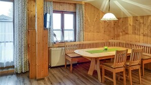 Una habitación con paneles de madera, una mesa redonda y bancos, un radiador y una ventana con cortinas.