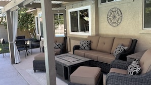 A covered patio area with a sectional sofa, wicker chairs, and a dining table. - Warm and inviting home centrally located. (La Quinta)