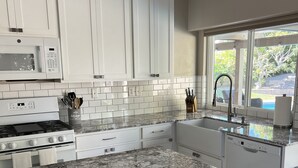 A modern kitchen with white cabinets, a granite countertop, a gas stove, and a view of a backyard through a large window. - Warm and inviting home centrally located. (La Quinta)