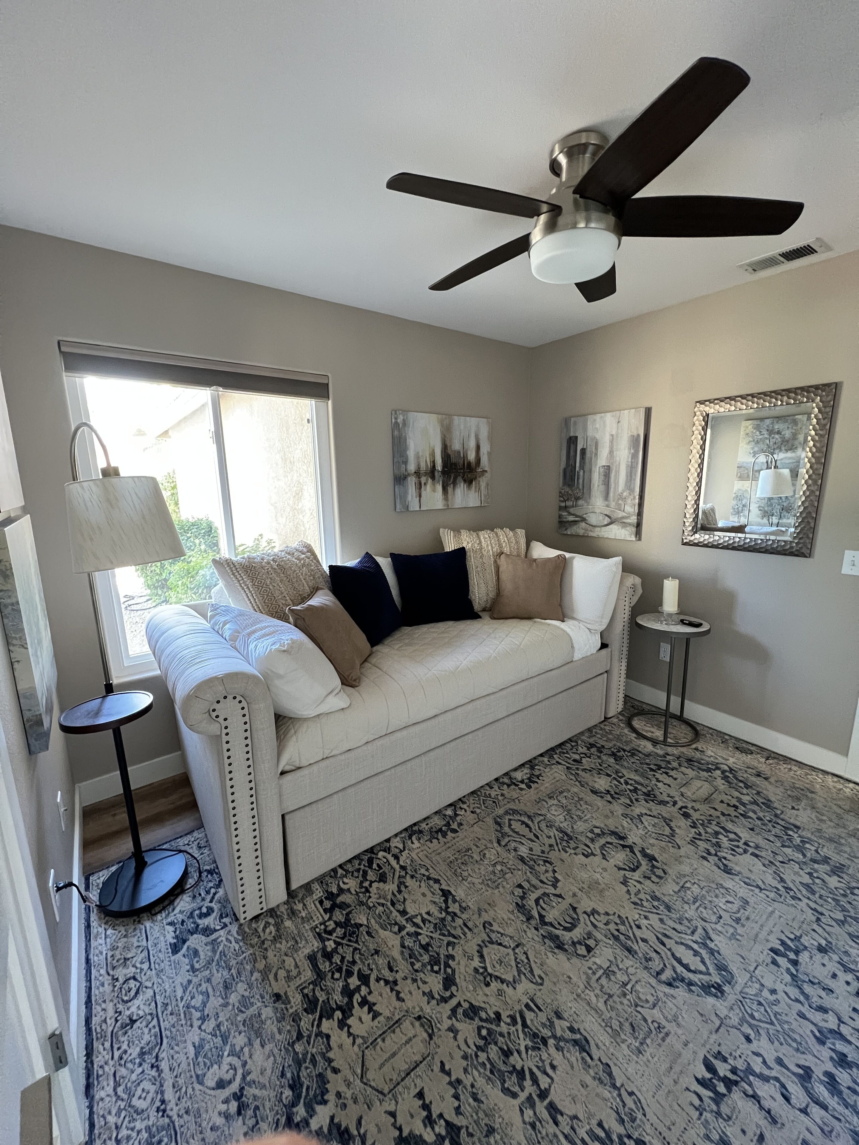 A living room with a beige sofa, a patterned rug, a ceiling fan, and artwork on the walls.