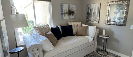 A living room with a beige sofa, a patterned rug, a ceiling fan, and artwork on the walls.