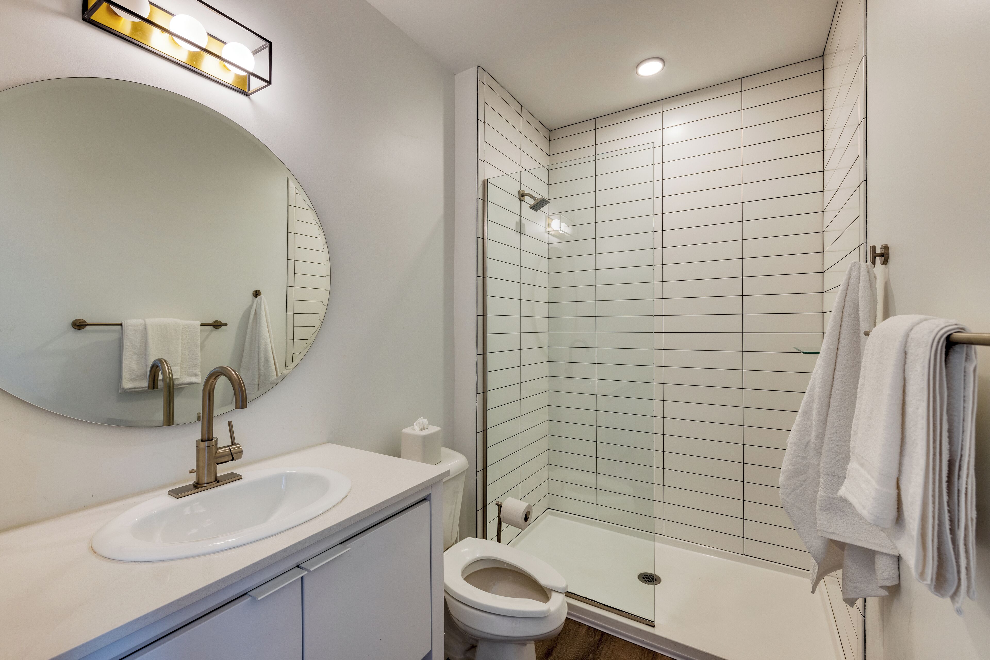 Une salle de bain moderne équipée d’un lavabo, d’un miroir, de toilettes et d’une douche à parois en verre.