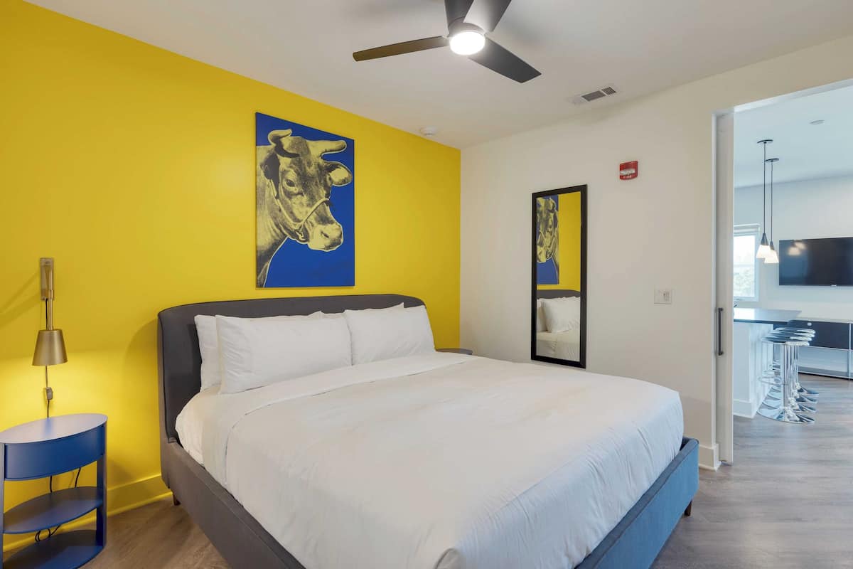 A modern hotel room with a large bed, a ceiling fan, and a bright yellow accent wall.