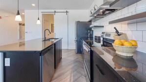 A modern kitchen with a central island, black cabinetry, and a stainless steel refrigerator. - The Carter by AvantStay (Nashville)