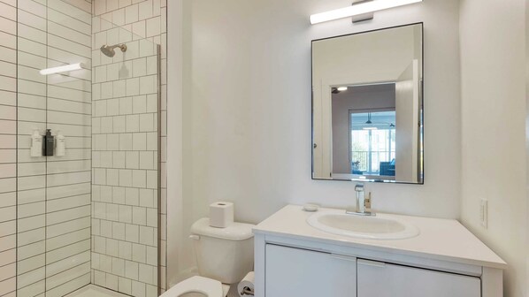 A modern bathroom with a glass shower enclosure, a white sink with a mirror above it, and a toilet with a roll of toilet paper.