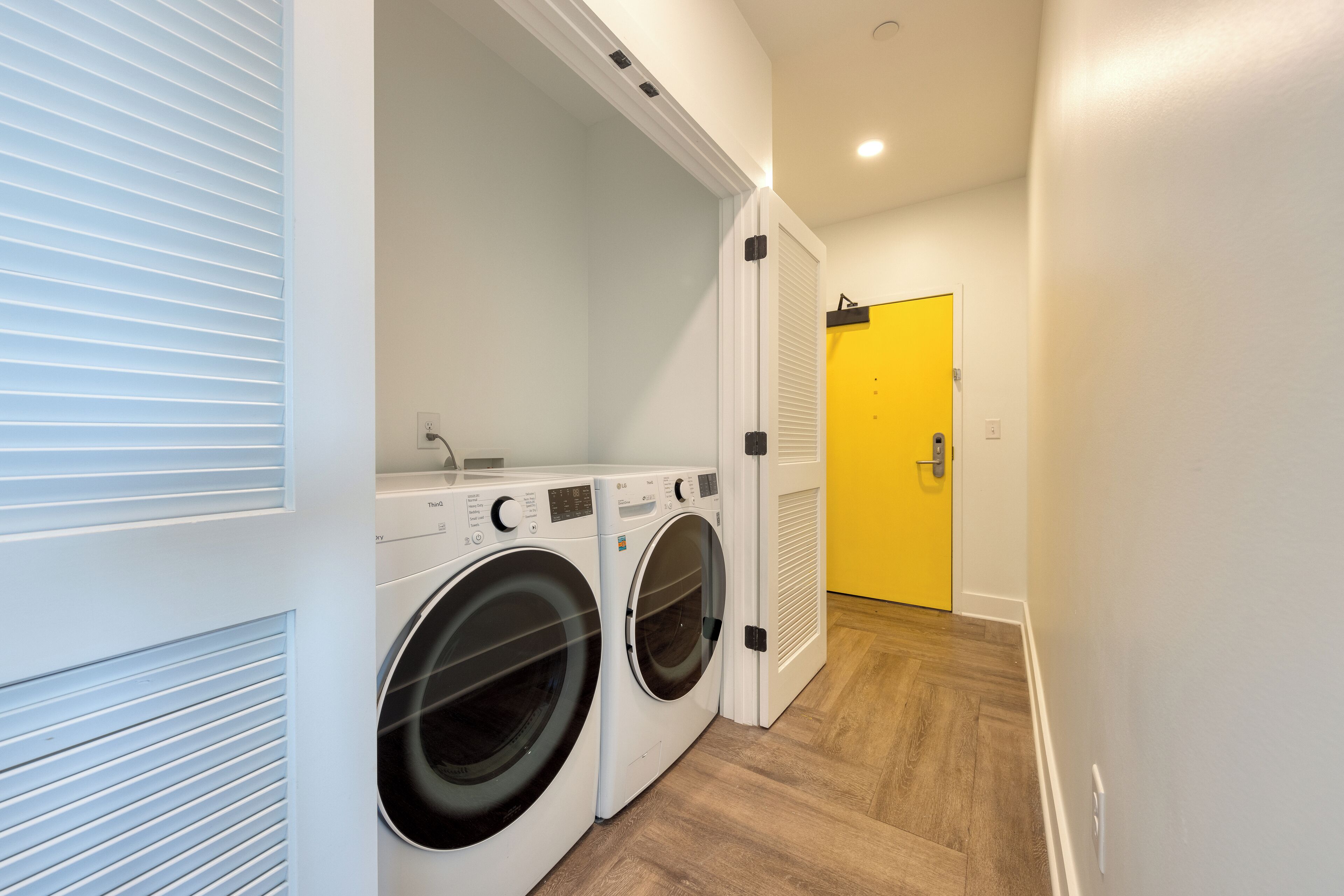A laundry area with two front-loading washing machines, a yellow door, and a wooden floor.