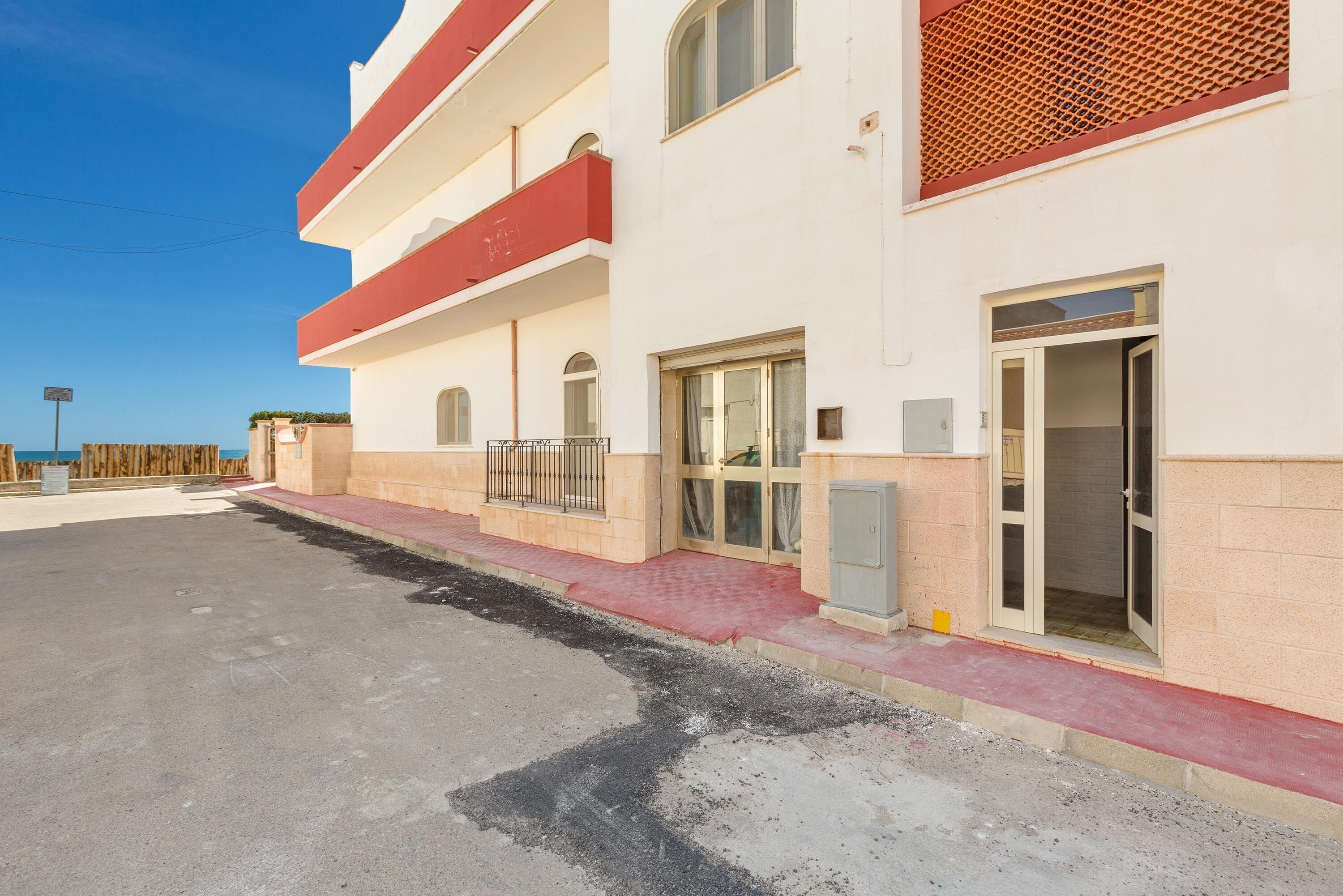 A multi-story building with a red balcony, a gated entrance, and a paved walkway.