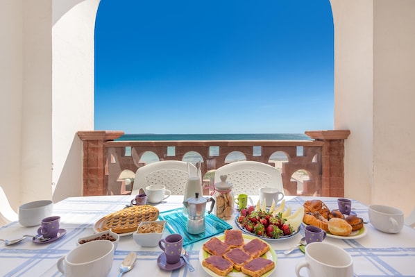 A table set for breakfast with various food items and cups, overlooking a clear blue sky.