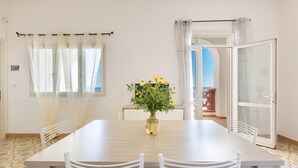 A dining area with a wooden table, white chairs, a vase with yellow flowers, and a view of the outdoors through a glass door. - 2854 Residence Bellavista - App 6 PP Fronte Mare by Barbarhouse (Porto Cesareo)