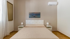 Una camera d'albergo con un letto, due comodini con lampade, un quadro appeso al muro e un condizionatore d'aria.