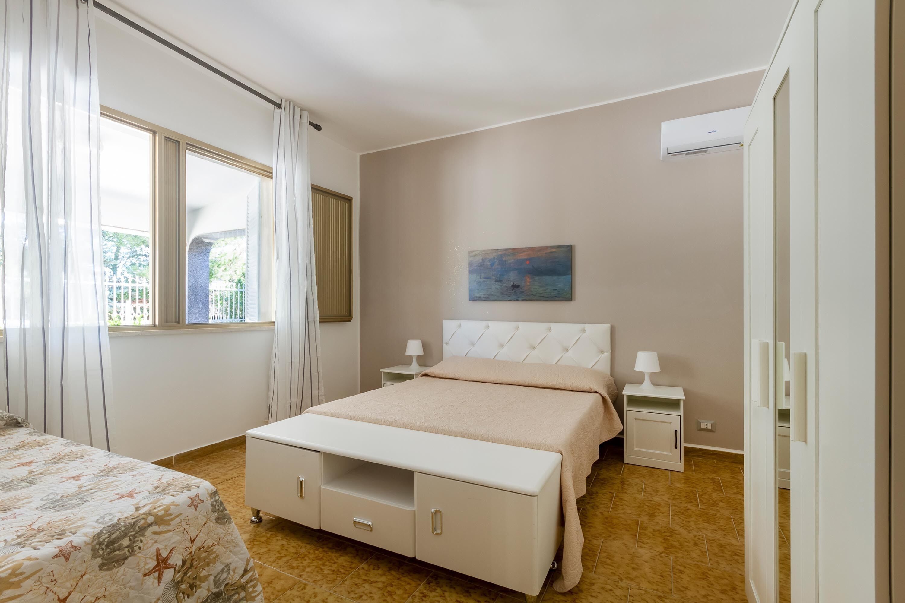 A bedroom with a bed, bedside tables, a painting, and a window with curtains.