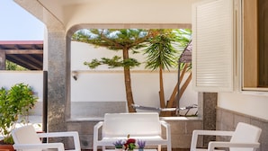 Un patio con sedie di plastica bianca, un tavolino con piante in vaso e un'amaca.