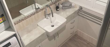 A bathroom with a sink, mirror, and a washing machine.