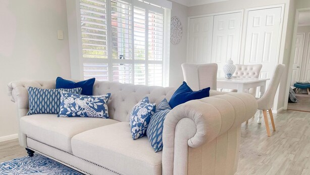 Een zithoek met een beige bank, kussens met een blauw-wit patroon, een passend blauw-wit vloerkleed en een witte eettafel met stoelen.