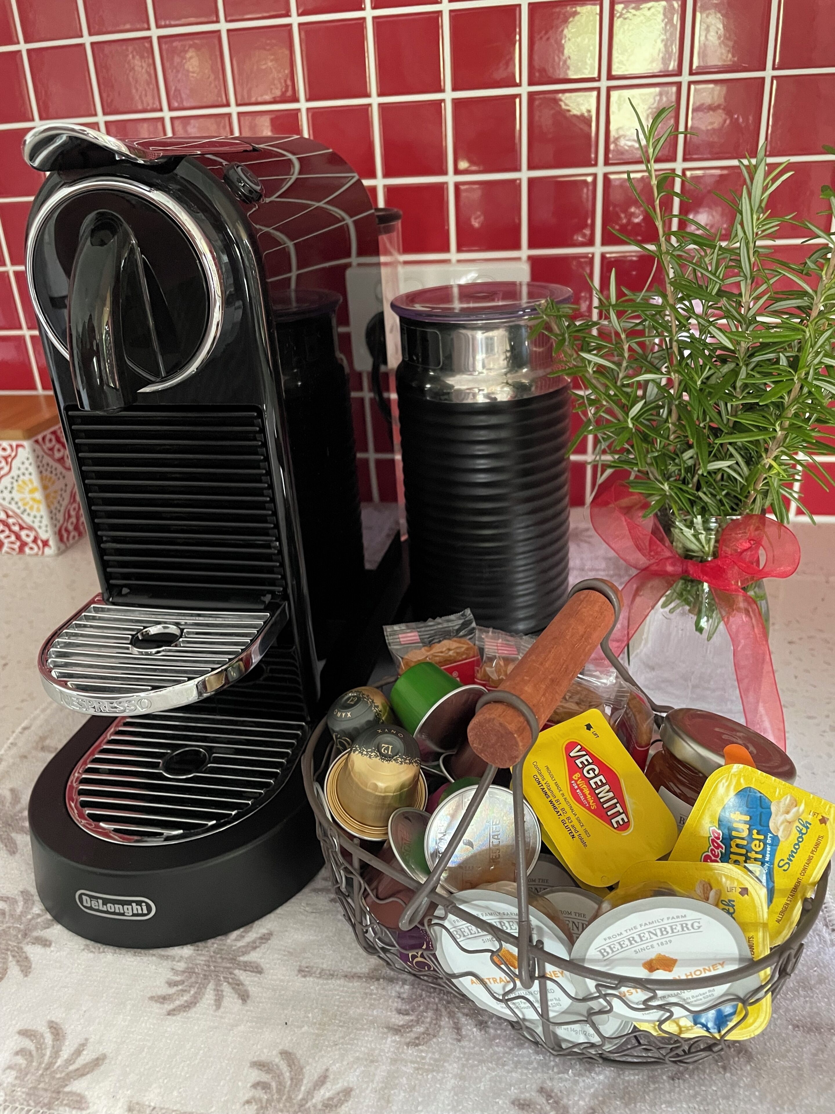 Eine Küchenzeile mit Kaffeemaschine, Thermoskanne, einem Honigglas, einer Korb voller Lebensmittel und einer Topfpflanze.