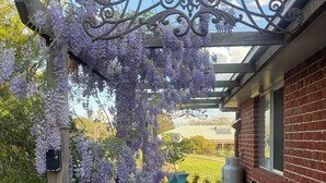 Een overdekt terras met een pergola, buitenmeubels en een bakstenen gebouw op de achtergrond.
