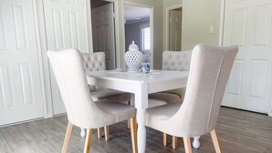 Een eetgedeelte met een witte tafel en vier beklede stoelen op houten poten.