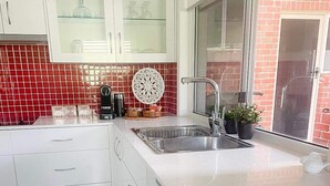 Een moderne keuken met witte kastjes, een roestvrijstalen spoelbak en een backsplash van rode tegels.