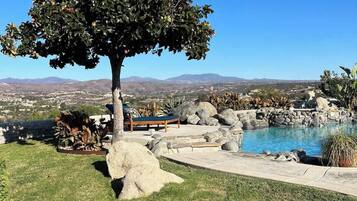 A tree-lined outdoor area with a pool, a lounge chair, and a view of distant mountains.