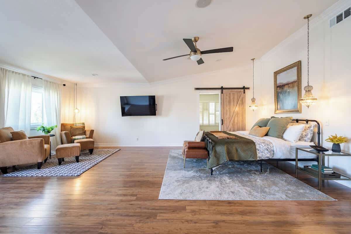 A spacious living room with a sofa set, a coffee table, a TV mounted on the wall, and a ceiling fan.