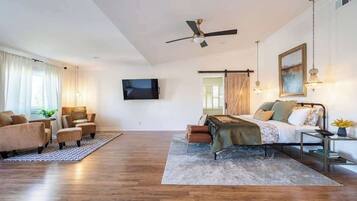 A spacious living room with a sofa set, a coffee table, a TV mounted on the wall, and a ceiling fan.