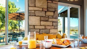A breakfast setting with stone walls, a dining table with plates, glasses, and a fruit bowl. - Hilltop Wine Estate- Pickleball | Pool | 360 views (Temecula)