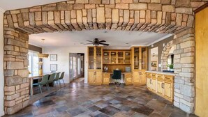 A spacious room with a stone archway, a dining area with chairs, a kitchen with wooden cabinets, and a ceiling fan. - Hilltop Wine Estate- Pickleball | Pool | 360 views (Temecula)