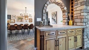 A dining area with a table and chairs, a stone archway, and a kitchen counter with cabinets. - Hilltop Wine Estate- Pickleball | Pool | 360 views (Temecula)