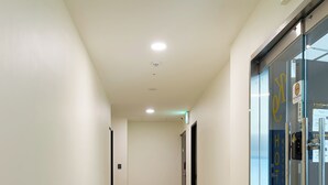 A clean, well-lit hotel corridor with a trash bin, a glass door with a sign, and a ceiling with recessed lighting. - K9 Myeongdong Seoul (Seoul)