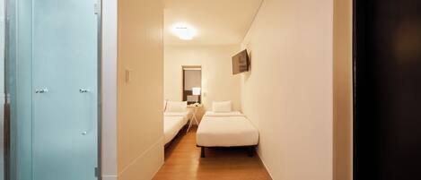 A narrow hallway with two beds, a door, and a mirror.