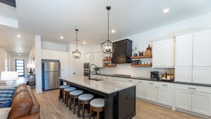 Una cocina moderna con armarios blancos, un refrigerador de acero inoxidable y una isla central con taburetes de bar.