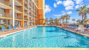 Een hotel met een zwembad, meerdere balkons en palmbomen.