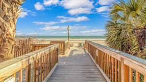 Een houten looppad naar een strand, met een heldere lucht.
