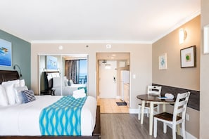 A hotel room with a bed, a desk, a chair, a small table, and a balcony view.