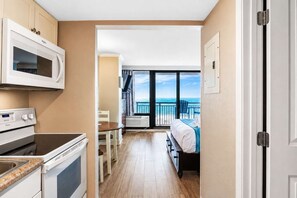 A compact hotel room with a kitchenette, a bed with a view, and a balcony.