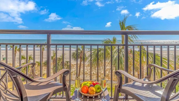 A balcony with two chairs, a table with fruit and a glass, and a view of the beach and ocean. - Ocean Reef 303 (Myrtle Beach)