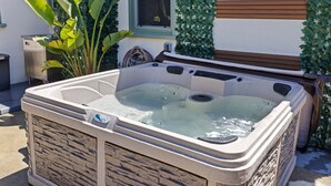 A hot tub with a stone exterior, positioned outdoors near a house with a window and green plants. - Old Town Monrovia Hot Tub Retreat (Monrovia)